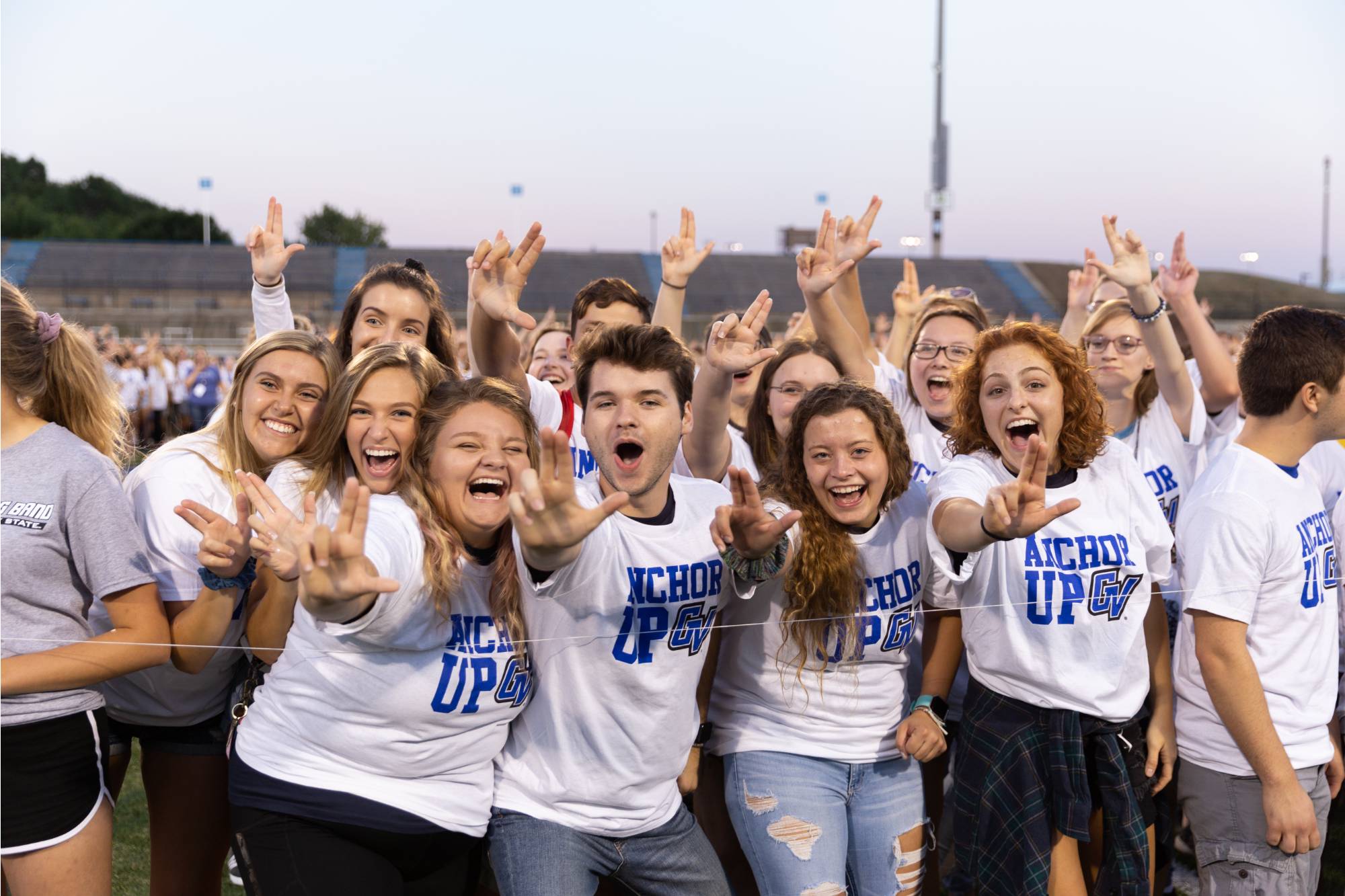 GVSU students attending a football game and showing "Laker Up" hand sign